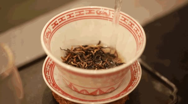 Air panas dituang ke daun teh kering dalam gaiwan porselen