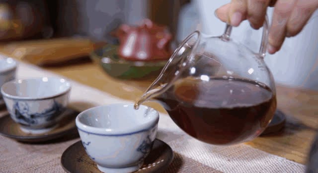 Daun teh hijau bergerak dalam seduhan kaca bening