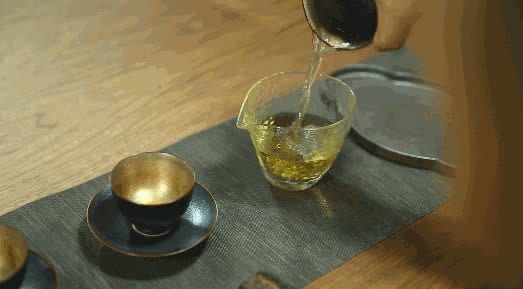 Teh dituang dari teko ke pitcher kaca, busa terbentuk di permukaan